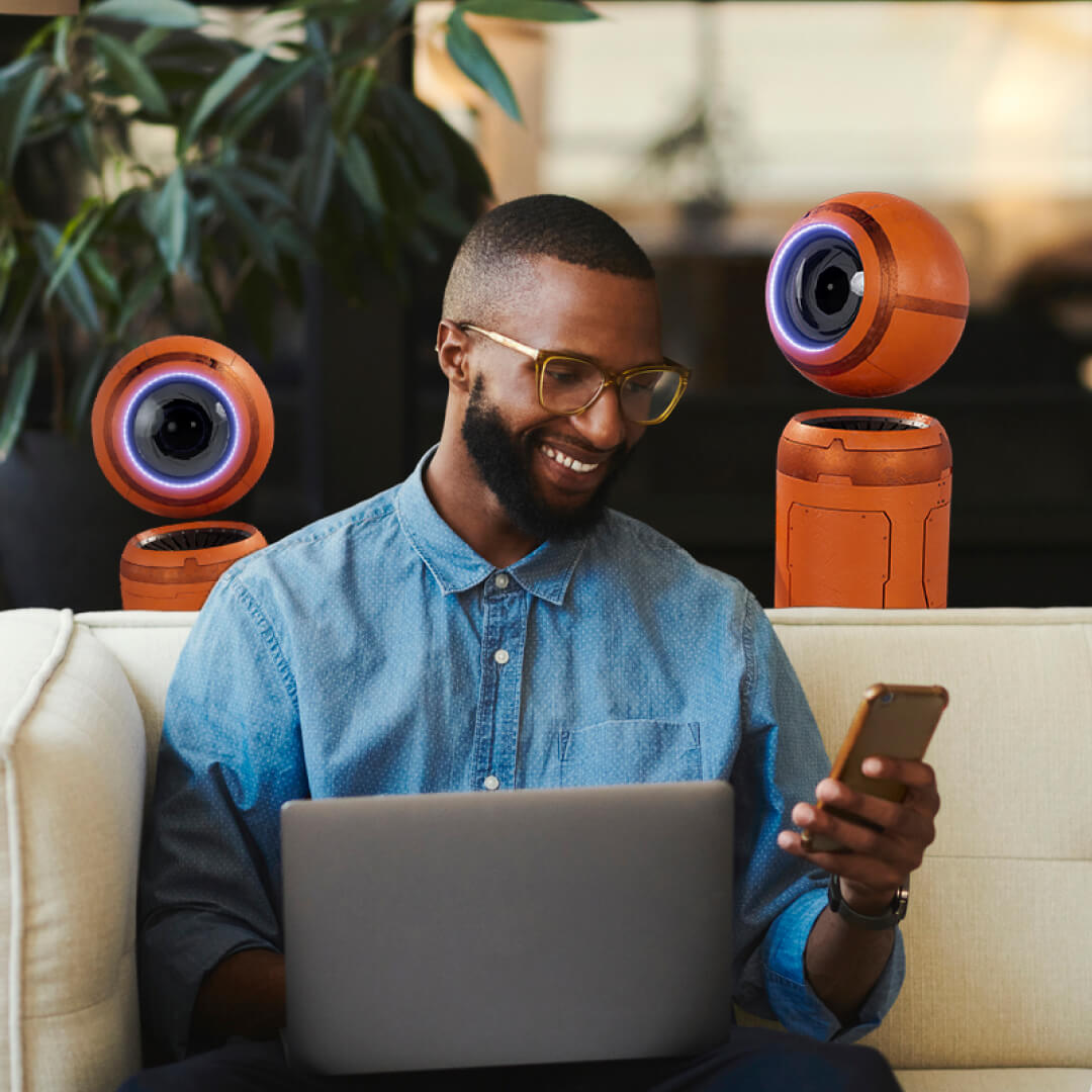 man on sofa looking at devices robots behind