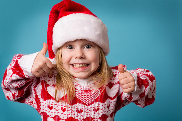 Girl wearing a Santa hat and Christmas jumper, making the thumbs up sign