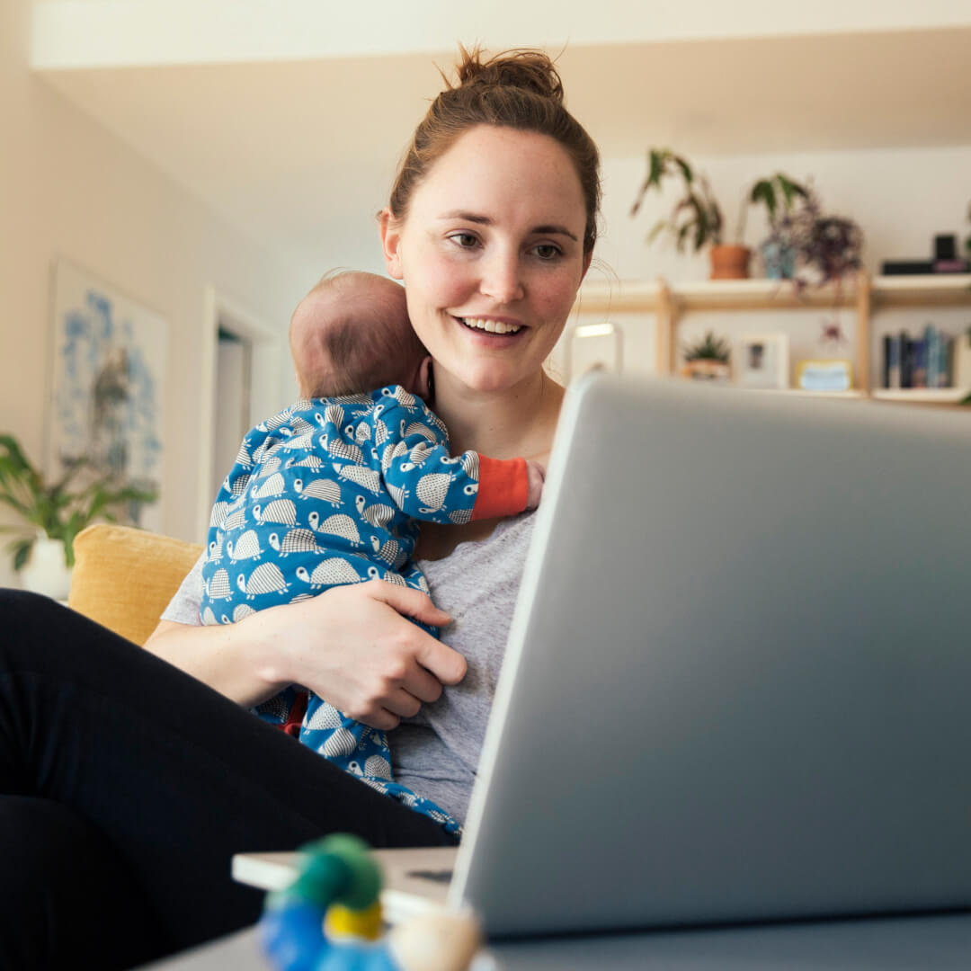 woman holding baby while investing on laptop