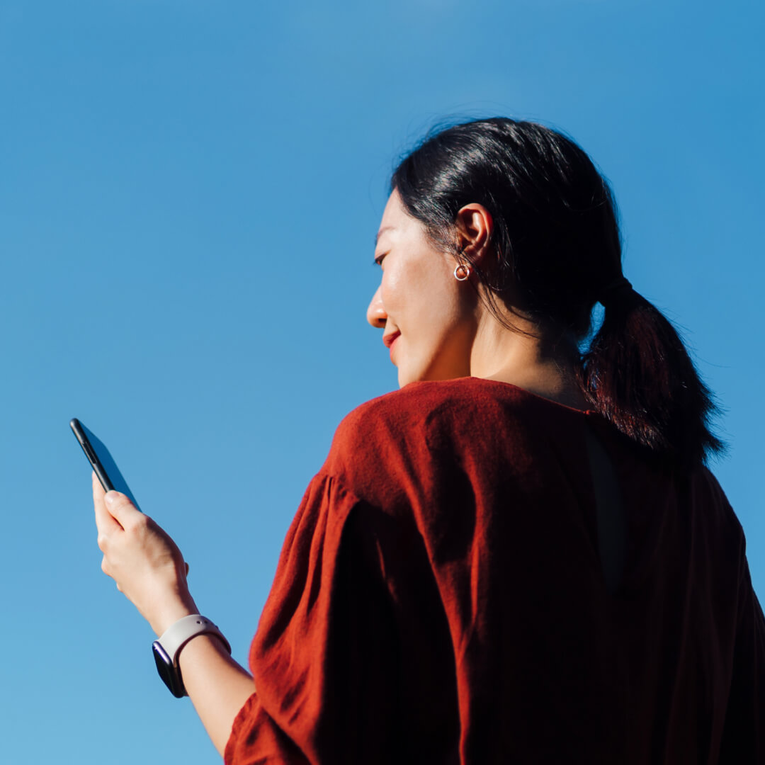 woman looking at mobile device in front of blue sky